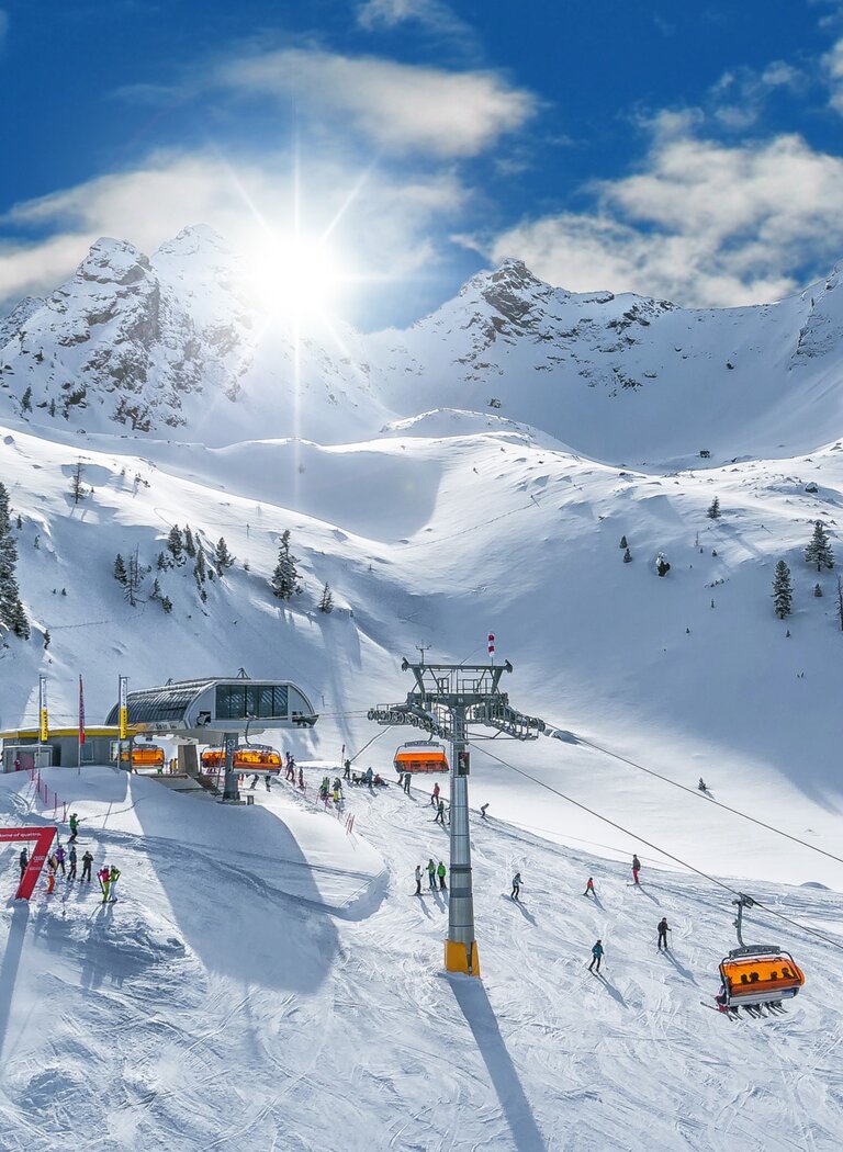 Skifahrer bei strahlendem Sonnenschein, oranger Sessellift vor verschneiten Berghängen und tiefblauem Himmel. | © SCHLADMING-DACHSTEIN Tourismusmarketing GmbH