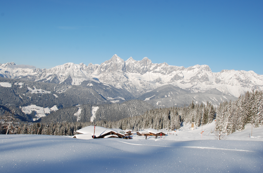 Snow-covered huts and forest with majestic alpine panorama under a clear blue sky. | © Reiteralm Bergbahnen GmbH & Co.KG