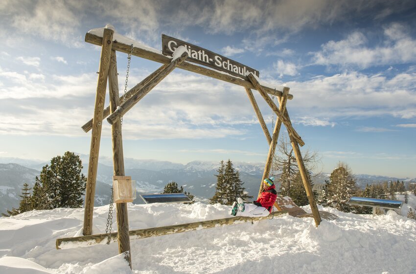 Child swinging on giant wooden swing in the snow with view of snowy mountain landscape. | © Reiteralm Bergbahnen GmbH & Co.KG