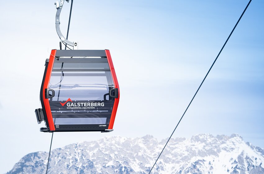 Red Galsterberg gondola glides through blue sky with snowy mountain backdrop in the Schladming-Dachstein region. | © Galsterbergalm Bahnen GmbH & Co KG 