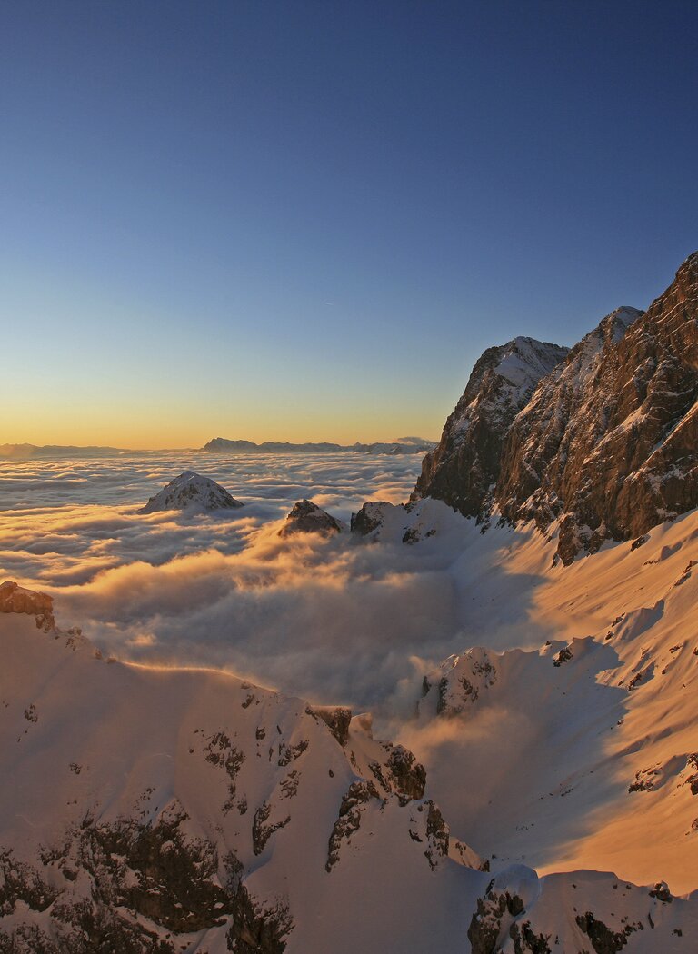 Sunset bathes the snowy south face and sea of clouds in warm alpenglow above the winter Alps. | © SCHLADMING-DACHSTEIN Tourismusmarketing GmbH