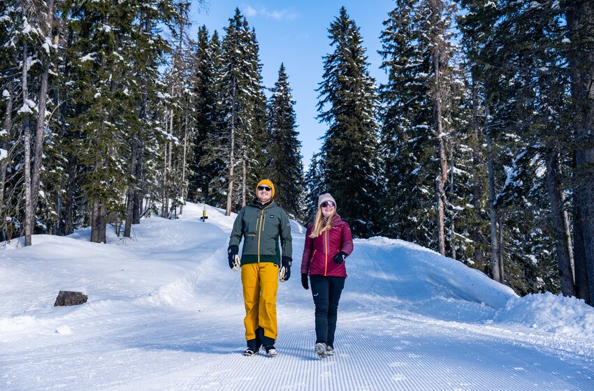 A couple walks on a groomed winter trail through snowy forest in bright sunshine and fresh alpine air. | © Winterwanderbilder (c) Gerald Oberreiter