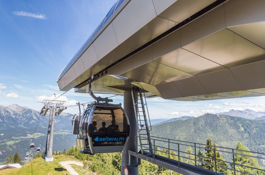 Modernes Gondellift-System auf der Reiteralm im Sommer | © Reiteralm Bergbahnen GmbH & Co.KG Gondel des Preunegg-Jet auf der Reiteralm schwebt aus moderner Bergstation über grüne Berghänge mit Alpenpanorama. | © Reiteralm Bergbahnen GmbH & Co.KG