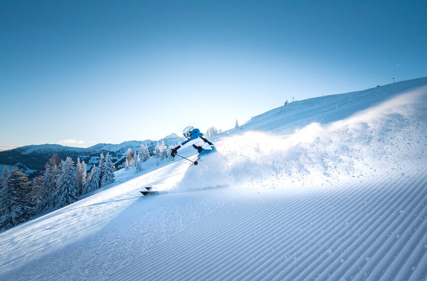 Ein Skifahrer zieht kraftvolle Schwünge durch frischen Pulverschnee auf einer sonnigen, präparierten Piste in Ski amadé. | © Ski amadé GmbH
